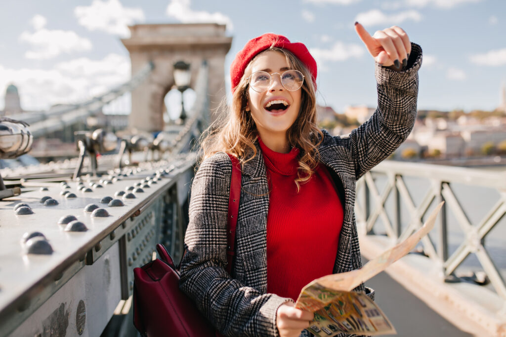 Enchanting female tourist exploring France with map. Outdoor portrait of happy brunette woman in red beret and glasses searching Paris attractions..